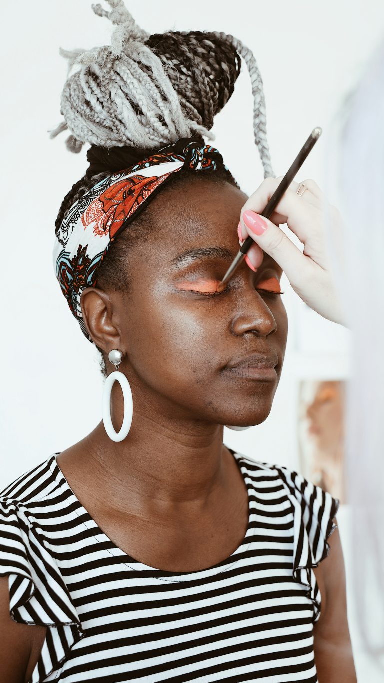 A Nigerian woman applying eyeliner or lipstick.